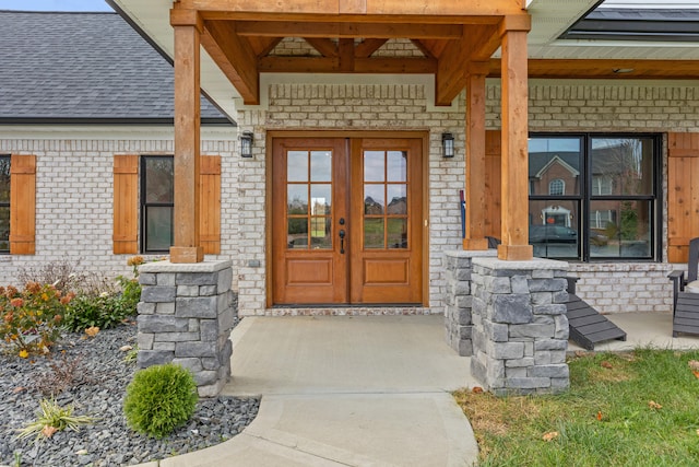 doorway to property featuring brick siding and roof with shingles