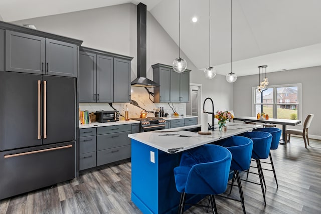 kitchen featuring backsplash, wall chimney range hood, decorative light fixtures, a center island with sink, and high quality appliances