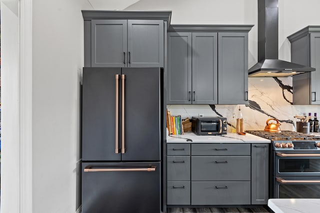 kitchen featuring backsplash, light stone counters, wall chimney exhaust hood, high quality appliances, and gray cabinets