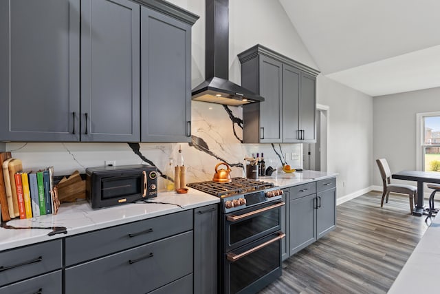 kitchen with light stone counters, gray cabinets, range with two ovens, and wall chimney range hood