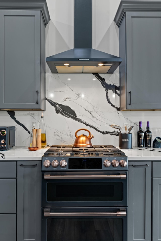 kitchen with decorative backsplash, gray cabinets, double oven range, and wall chimney range hood