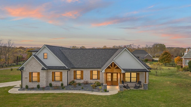 modern farmhouse style home featuring french doors, brick siding, a lawn, and fence