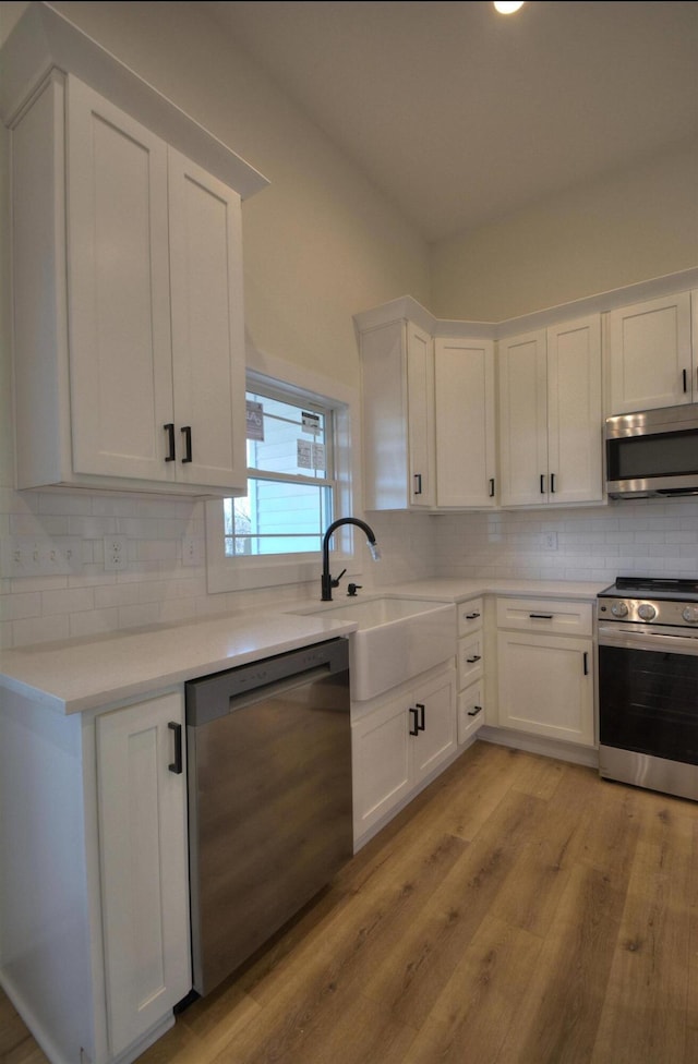 kitchen featuring sink, light hardwood / wood-style flooring, tasteful backsplash, white cabinetry, and stainless steel appliances