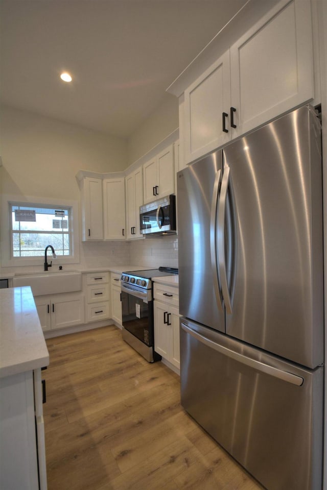 kitchen featuring sink, backsplash, light hardwood / wood-style floors, white cabinets, and appliances with stainless steel finishes