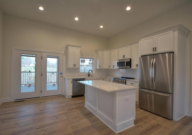 kitchen with sink, light hardwood / wood-style flooring, a kitchen island, white cabinetry, and stainless steel appliances