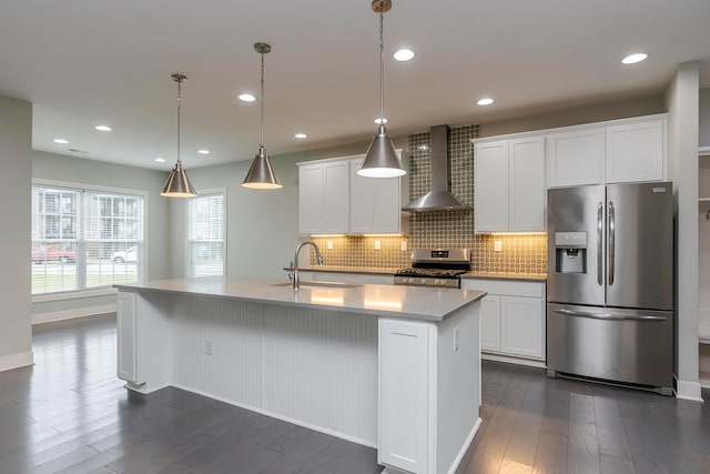 kitchen featuring appliances with stainless steel finishes, sink, wall chimney range hood, a center island with sink, and white cabinetry