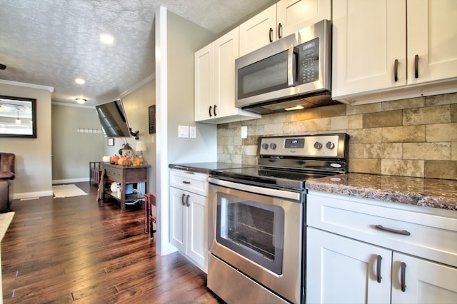 kitchen featuring white cabinetry, stainless steel appliances, dark stone counters, ornamental molding, and dark hardwood / wood-style floors