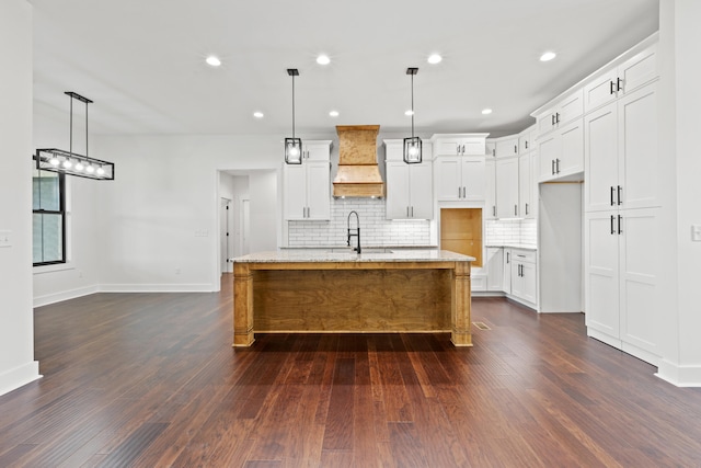 kitchen featuring pendant lighting, white cabinetry, custom exhaust hood, and a center island with sink