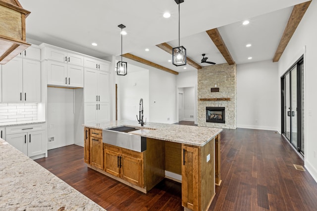 kitchen featuring pendant lighting, an island with sink, sink, white cabinets, and light stone countertops