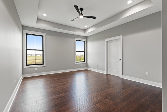 empty room featuring a raised ceiling, ceiling fan, and dark hardwood / wood-style flooring