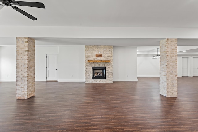 unfurnished living room with ornate columns, dark hardwood / wood-style flooring, a stone fireplace, and ceiling fan