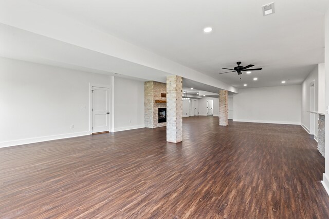 unfurnished living room with a stone fireplace, decorative columns, dark hardwood / wood-style floors, and ceiling fan