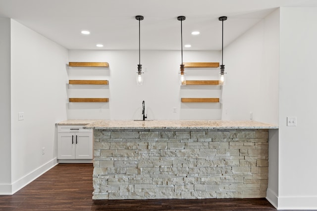 bar featuring sink, white cabinetry, light stone counters, decorative light fixtures, and dark hardwood / wood-style flooring