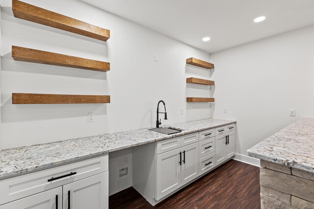 bar with sink, light stone counters, hanging light fixtures, dark hardwood / wood-style floors, and white cabinets