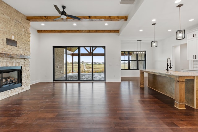 unfurnished living room featuring a stone fireplace, sink, dark wood-type flooring, and ceiling fan