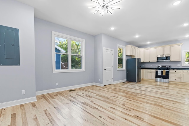 kitchen with light hardwood / wood-style floors, stainless steel appliances, cream cabinets, and electric panel