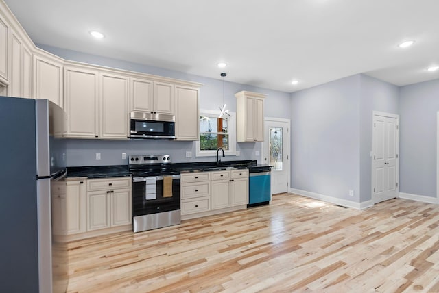 kitchen with cream cabinetry, sink, decorative light fixtures, light wood-type flooring, and appliances with stainless steel finishes