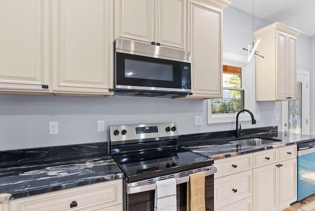 kitchen with hanging light fixtures, sink, cream cabinetry, light hardwood / wood-style floors, and stainless steel appliances