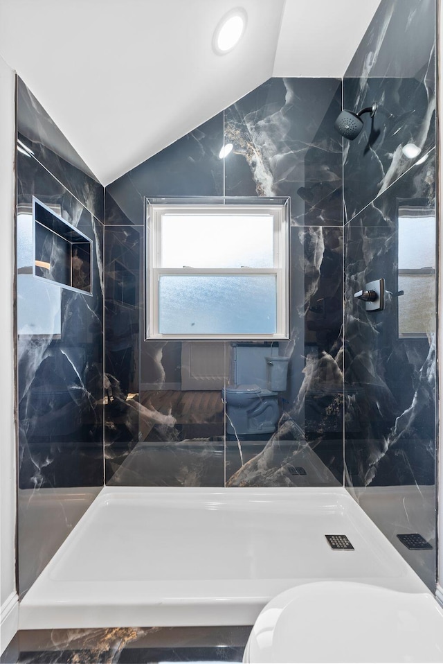 bathroom with tile walls, tiled shower, vaulted ceiling, and toilet