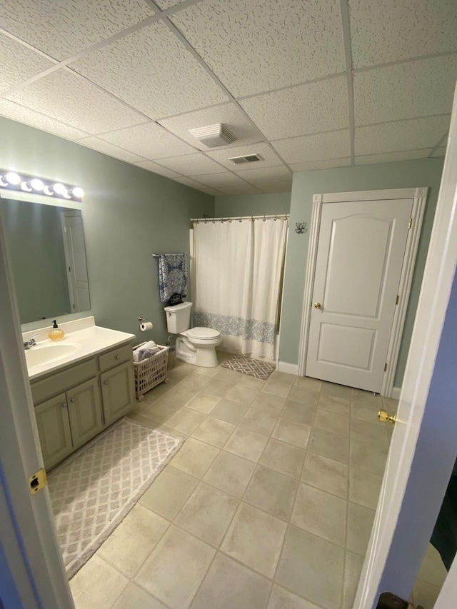 bathroom featuring tile patterned flooring, vanity, a drop ceiling, and toilet