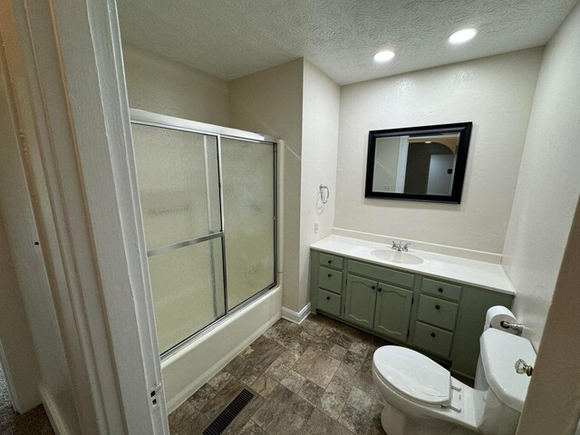 full bathroom with vanity, bath / shower combo with glass door, a textured ceiling, and toilet