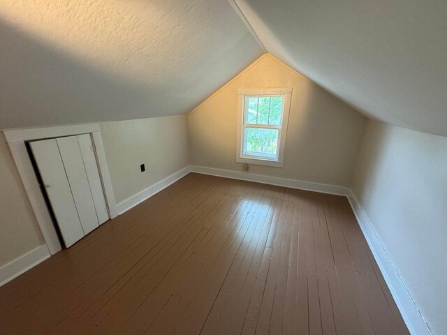 bonus room with lofted ceiling, dark wood-type flooring, and a textured ceiling