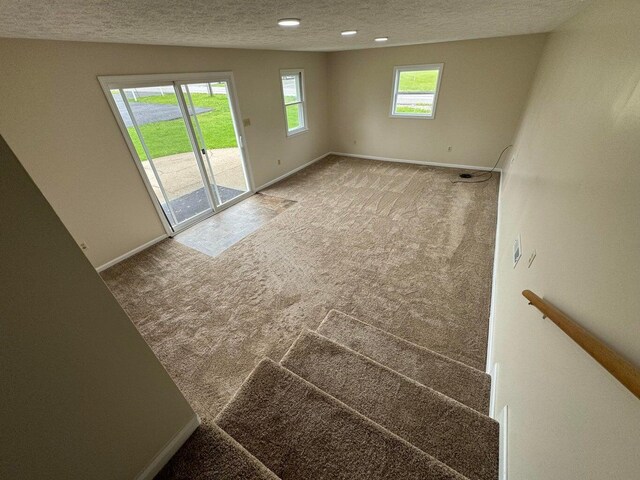 carpeted empty room featuring a wealth of natural light, lofted ceiling, and a textured ceiling