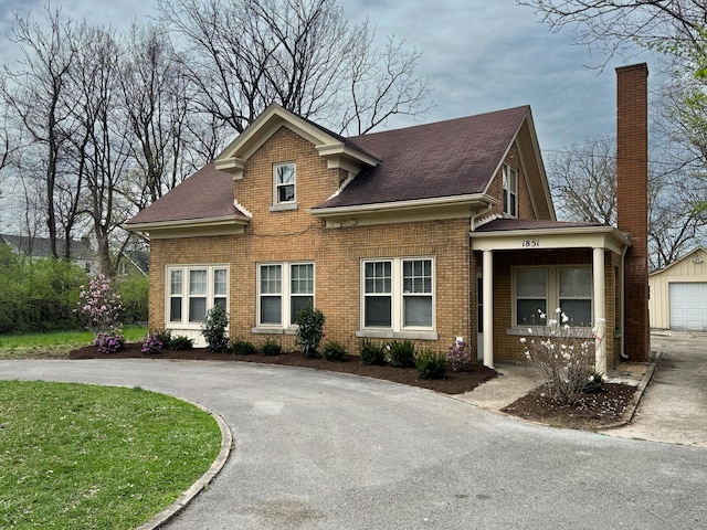 view of front facade with aphalt driveway, a chimney, an outdoor structure, and brick siding