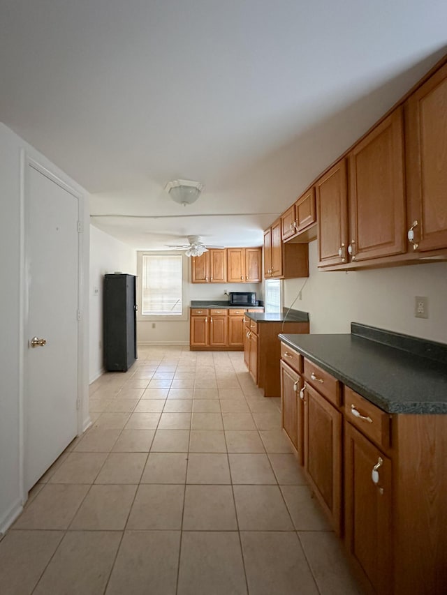 kitchen with light tile patterned flooring, a ceiling fan, brown cabinets, dark countertops, and black appliances