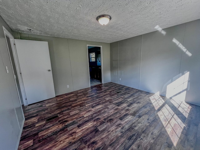 empty room with a textured ceiling and dark hardwood / wood-style floors