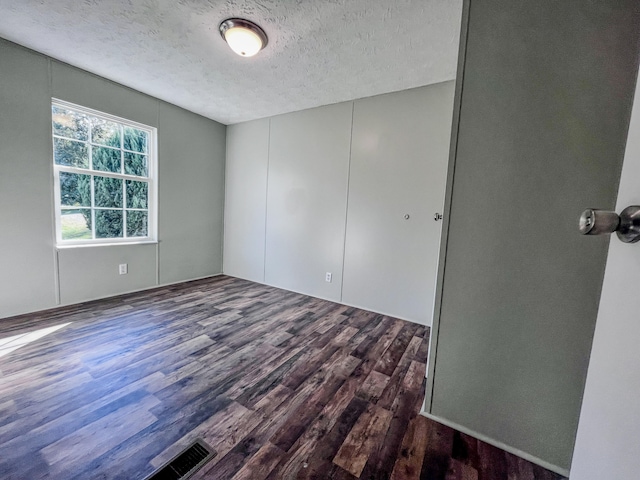 empty room with dark hardwood / wood-style floors and a textured ceiling