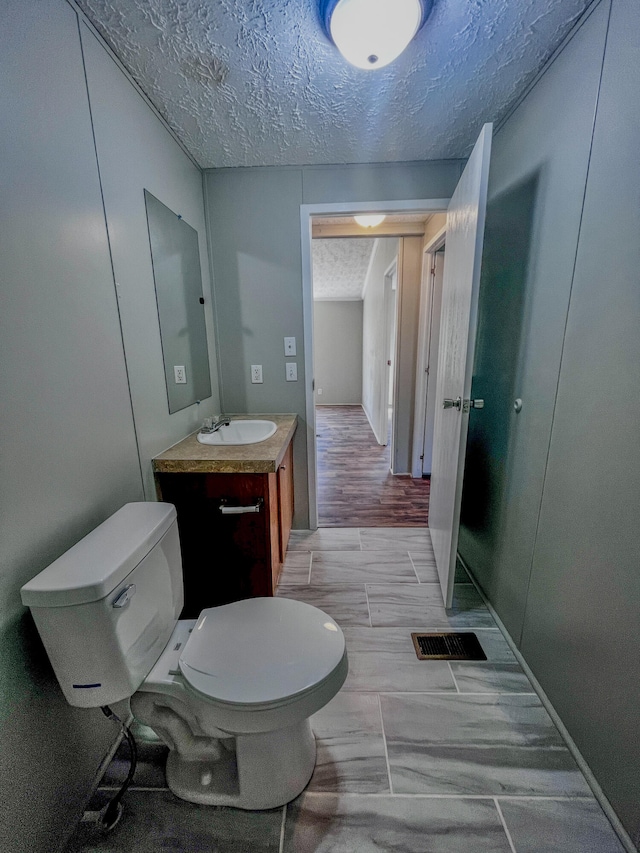 bathroom with hardwood / wood-style flooring, vanity, toilet, and a textured ceiling