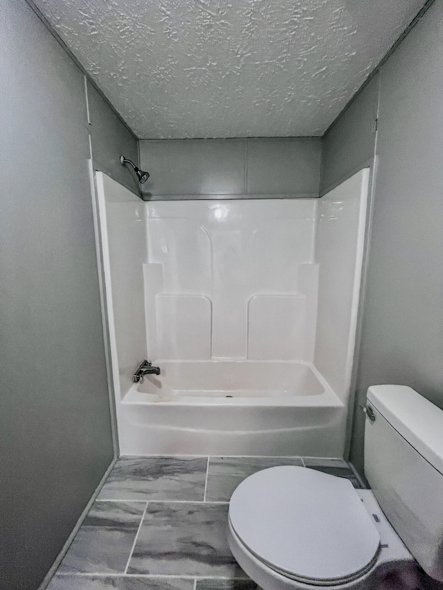 bathroom with a textured ceiling, toilet, and bathing tub / shower combination