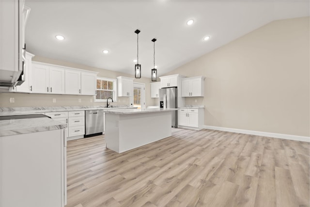 kitchen with appliances with stainless steel finishes, white cabinets, vaulted ceiling, a sink, and a kitchen island