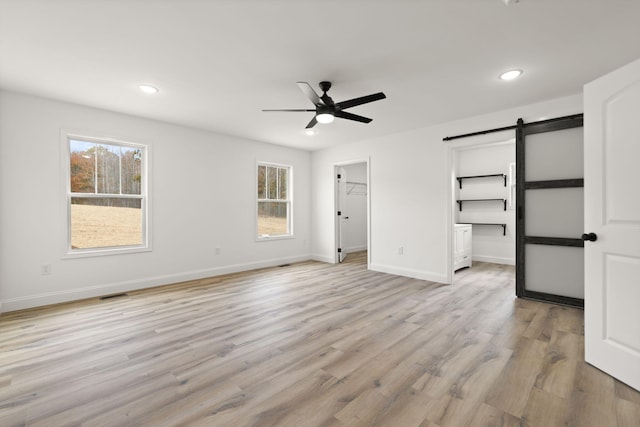 unfurnished bedroom with light wood finished floors, a spacious closet, a barn door, and multiple windows