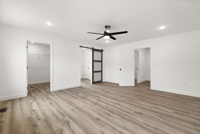 unfurnished bedroom with a barn door, baseboards, light wood-style flooring, and recessed lighting