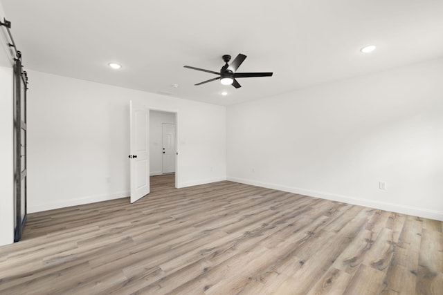 spare room featuring a barn door, recessed lighting, wood finished floors, a ceiling fan, and baseboards