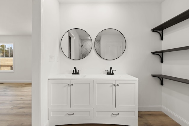 bathroom with double vanity, a sink, baseboards, and wood finished floors