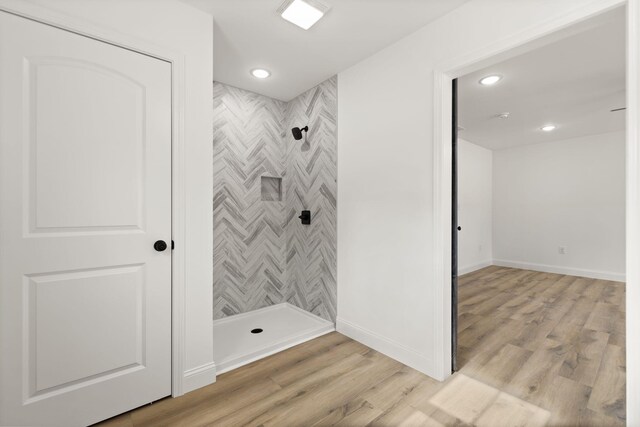 bathroom with tiled shower, wood finished floors, and baseboards