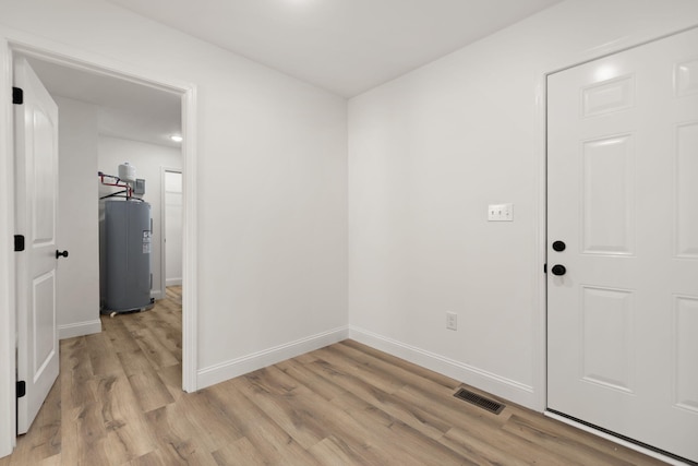 empty room with visible vents, light wood-type flooring, electric water heater, and baseboards