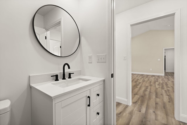 half bath with toilet, baseboards, wood finished floors, and vanity