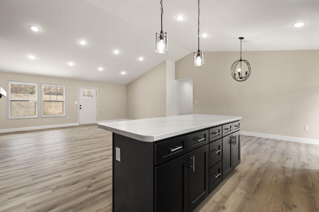 kitchen with lofted ceiling, light wood-style flooring, a kitchen island, light countertops, and dark cabinetry