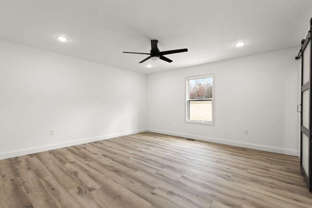 spare room featuring recessed lighting, a barn door, ceiling fan, wood finished floors, and baseboards