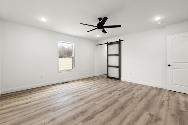 spare room with a barn door, baseboards, ceiling fan, light wood-type flooring, and recessed lighting