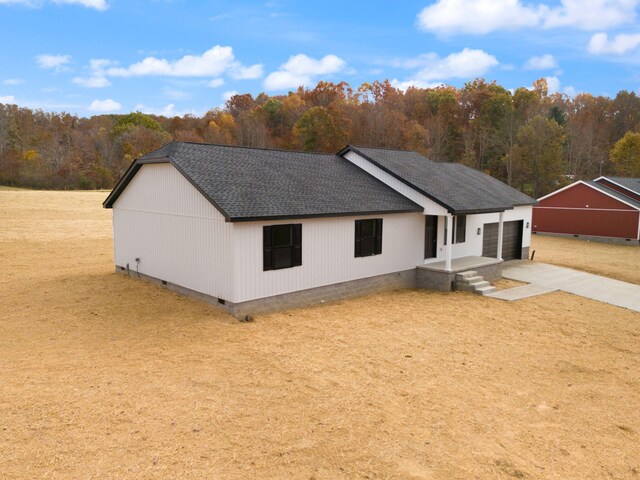 view of front of home with an attached garage, concrete driveway, crawl space, roof with shingles, and a wooded view