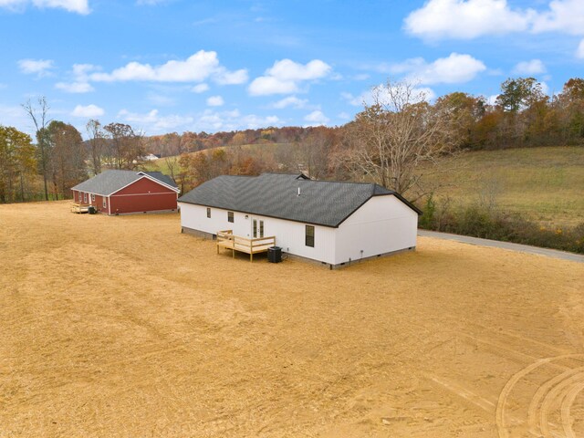 rear view of property with a forest view, dirt driveway, a pole building, and an outdoor structure