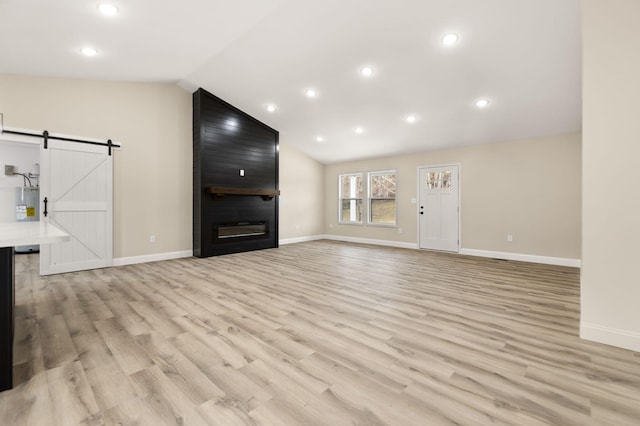 unfurnished living room featuring a barn door, baseboards, vaulted ceiling, light wood-style floors, and a fireplace