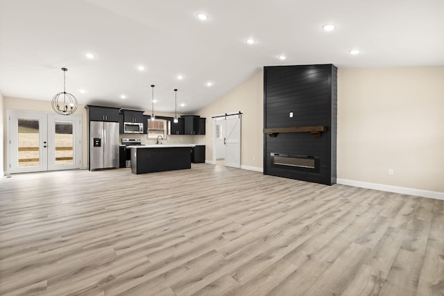 kitchen with light countertops, a barn door, appliances with stainless steel finishes, open floor plan, and an island with sink