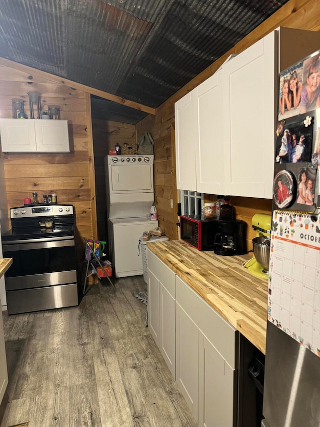 kitchen with wood walls, stainless steel range with electric cooktop, wood counters, stacked washer and dryer, and white cabinets