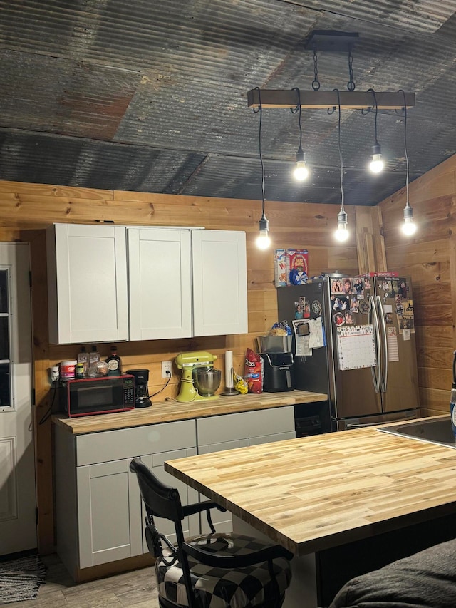 kitchen with butcher block counters, a breakfast bar area, wooden walls, stainless steel refrigerator with ice dispenser, and pendant lighting